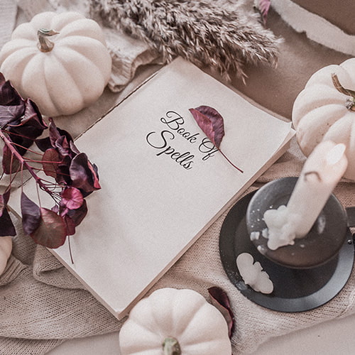 A table with a candle, book of spells, white pumpkins and dried leaves and flowers