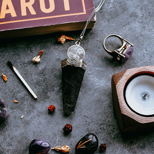 A table with a tarot book, a candle, crystal ring, crystal necklace, crystal tumbles and dried flowers